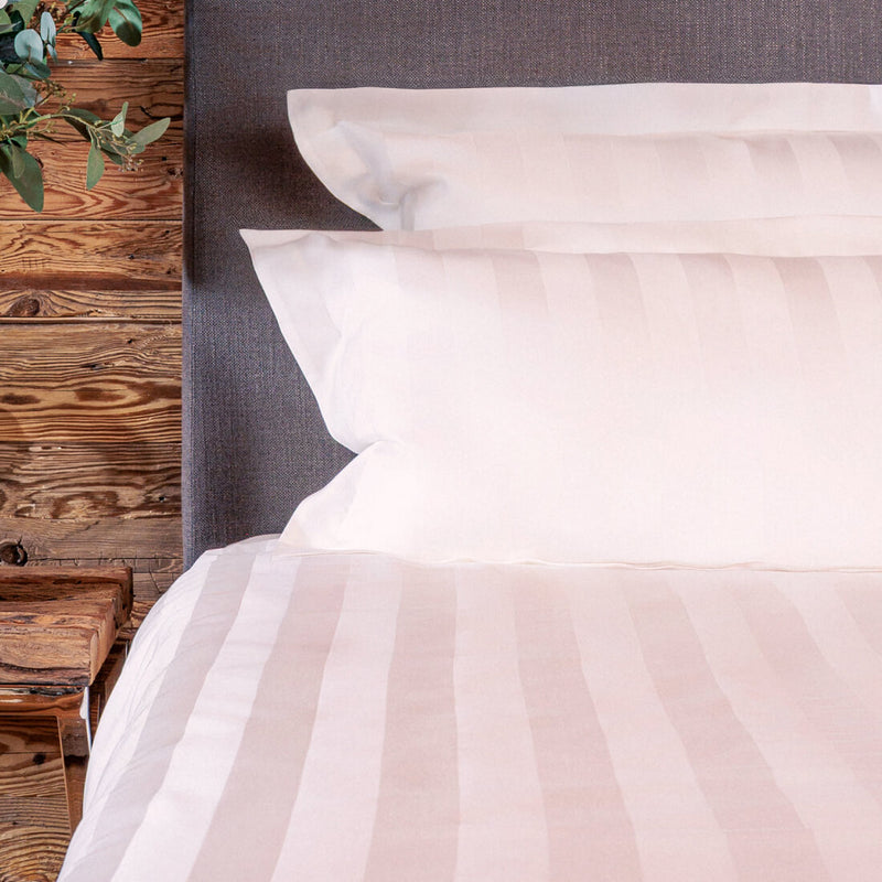 Close-up of a bed with white bedding and pillows against a wooden headboard.