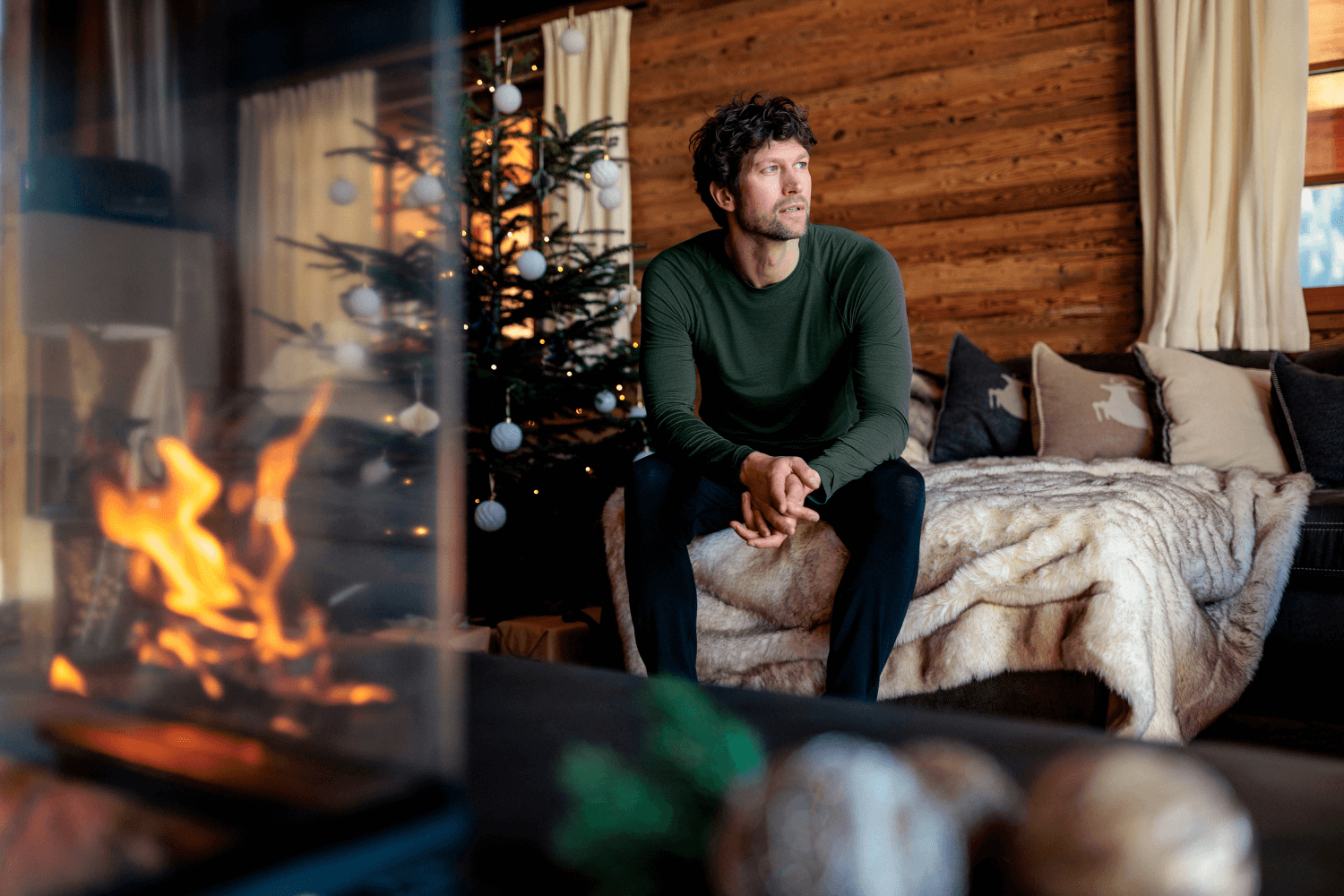 Man sitting on a couch by a fireplace in a cozy living room with Christmas decorations.
